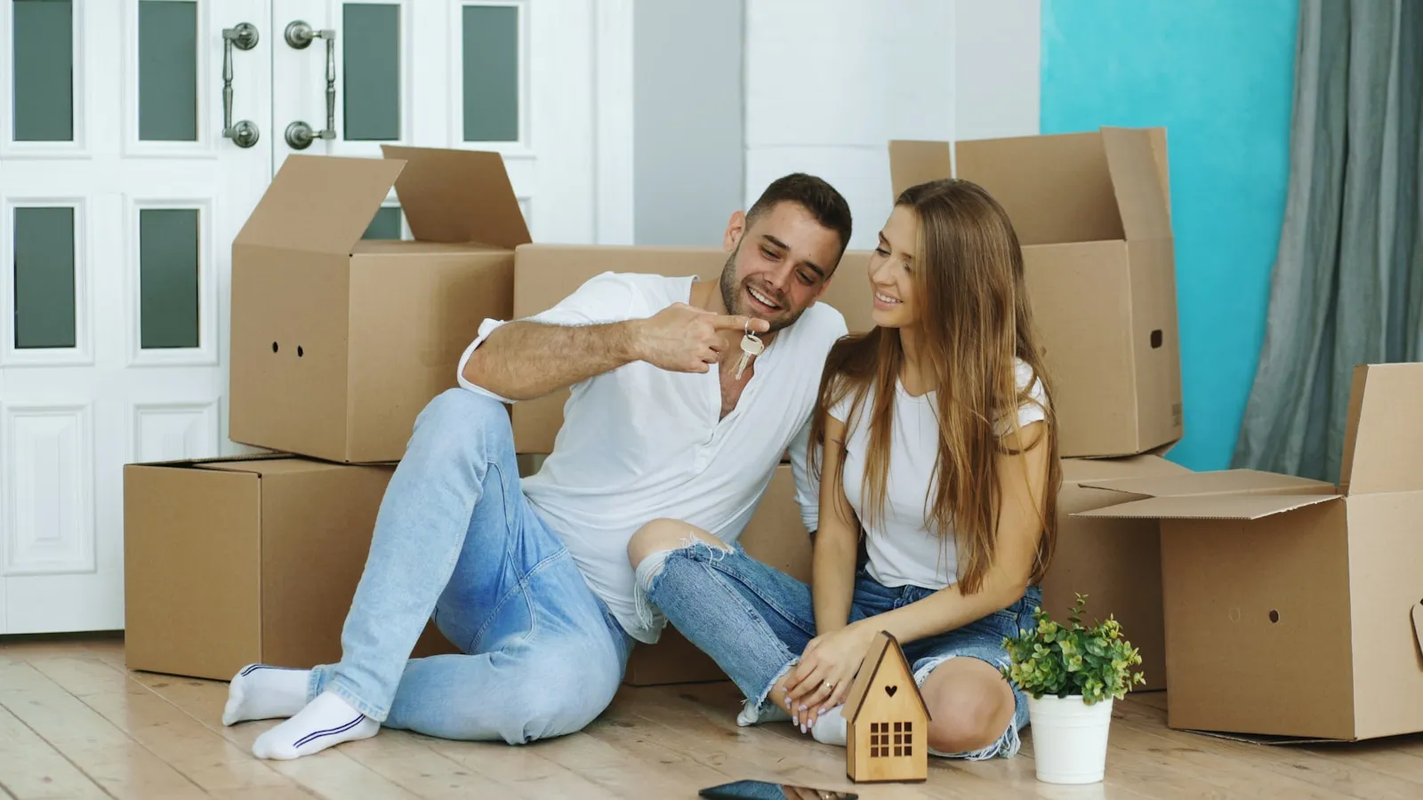 Young couple sitting on the floor of their new home with house keys and moving boxes