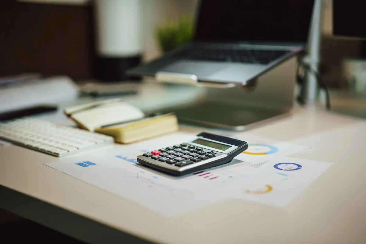 A calculator, laptop and printed figures on a desk