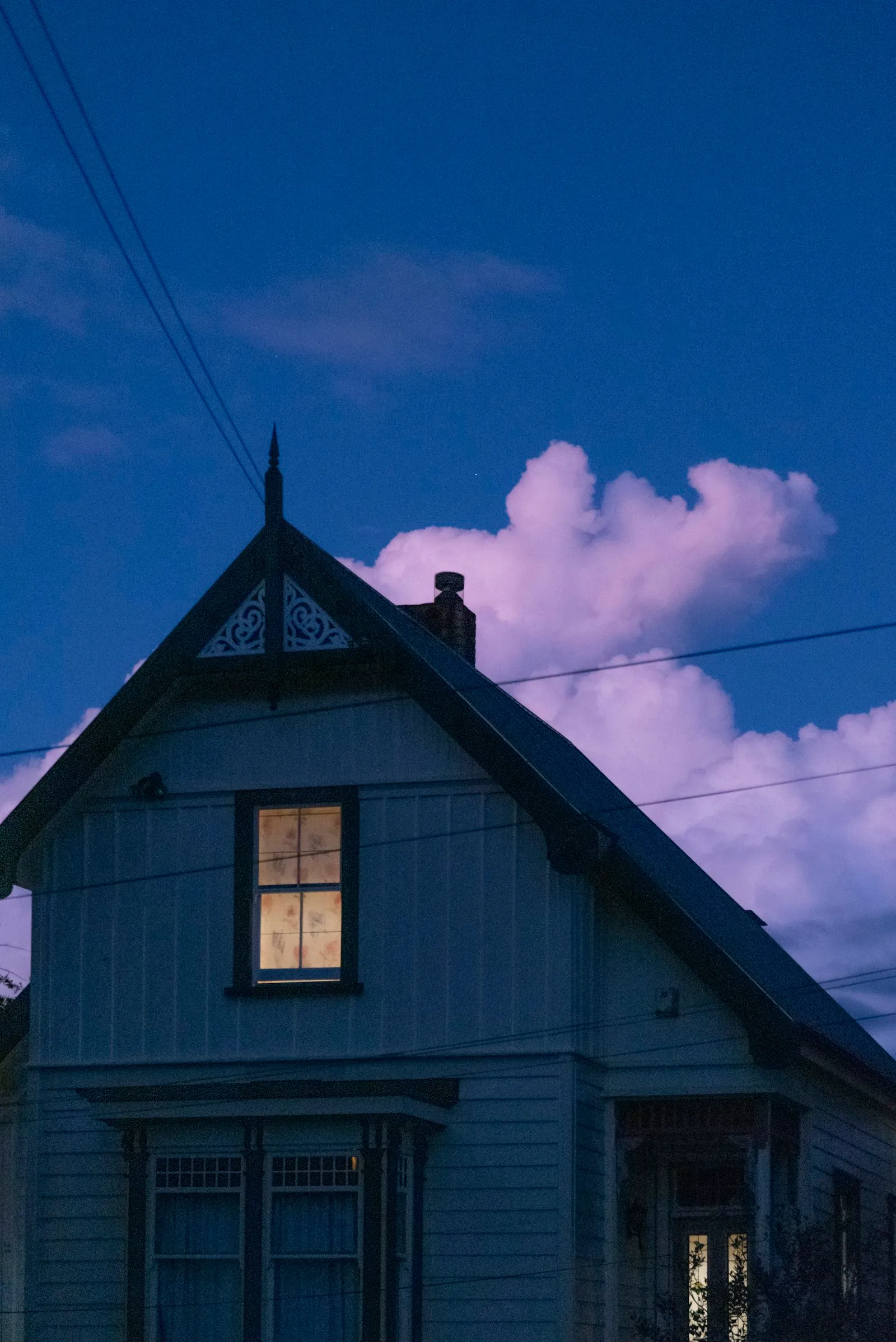 An Auckland villa lit from within at dusk, a single upstairs window glowing against a deep blue sky