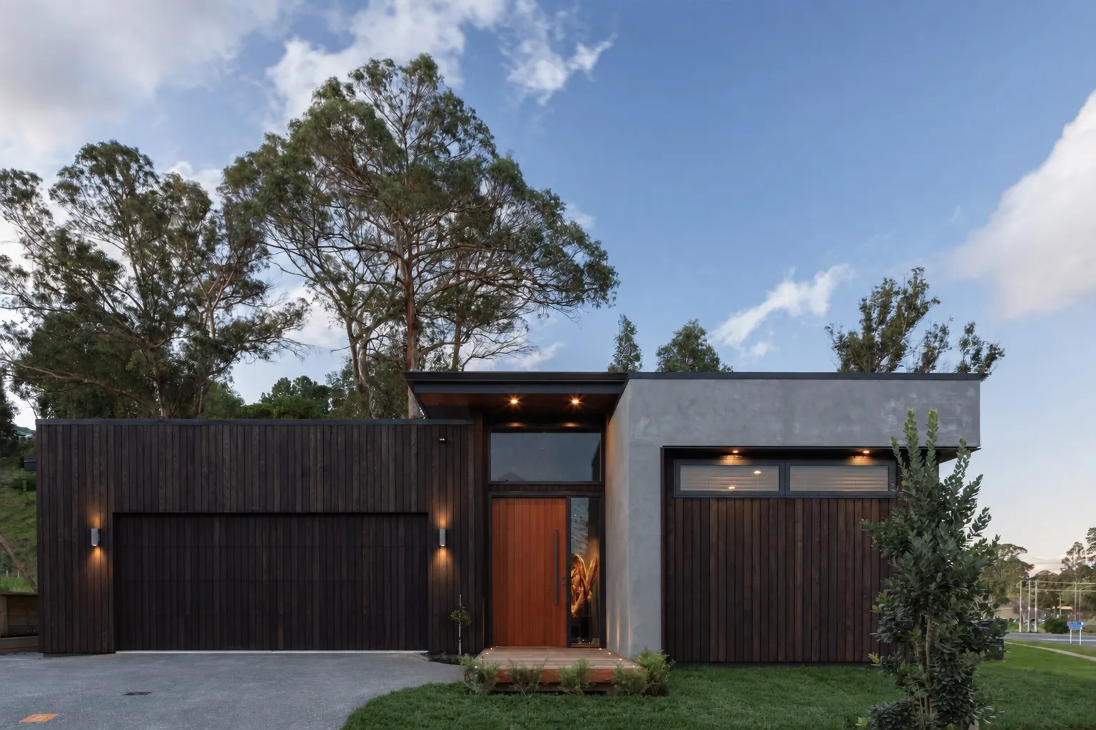 A premium architectural New Zealand home with dark timber cladding, lit at dusk