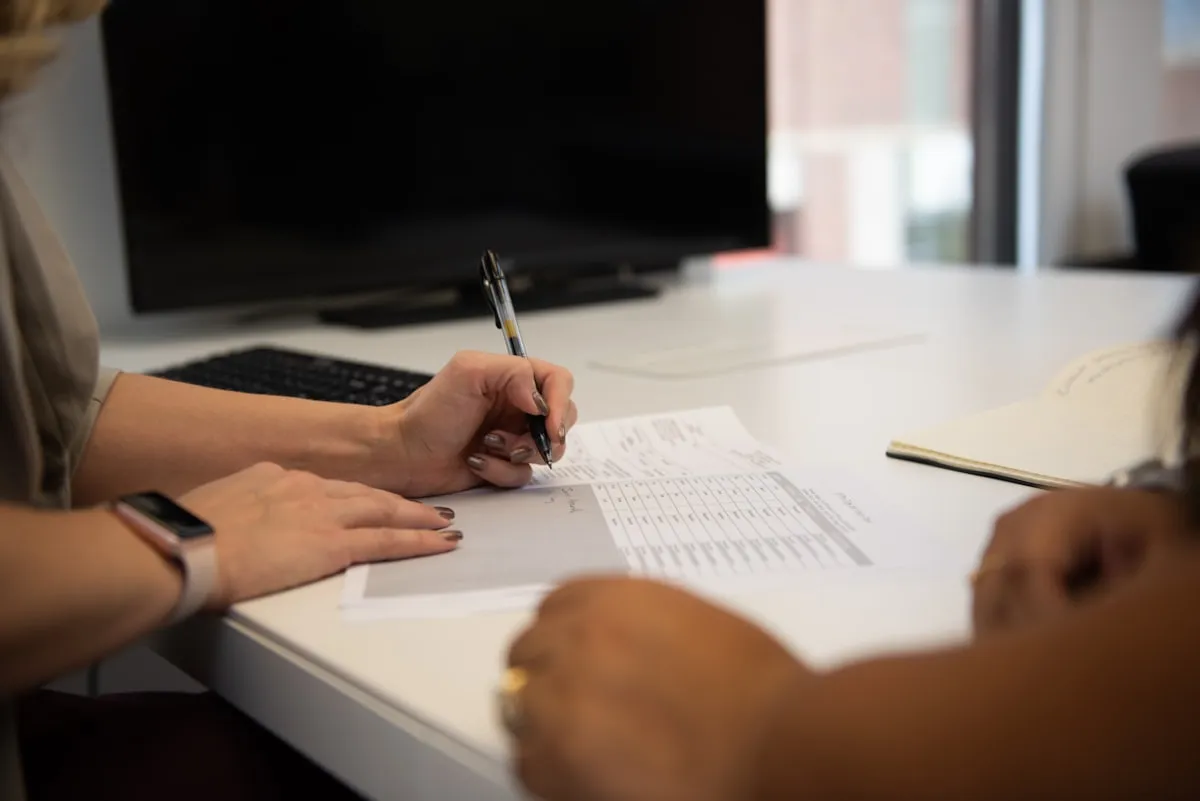 Two people at a desk reviewing and signing a printed document with a table of figures